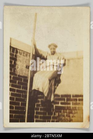 Stampa fotografica di una donna su una parete di mattoni. Una stampa fotografica di una donna non identificata. La donna è raffigurata tenendo su un palo e appoggiandosi contro un muro di mattoni. Sul retro della fotografia è stampato [39] con inchiostro nero. Foto Stock