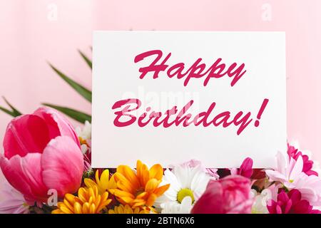 Felice testo di compleanno sulla carta in bouquet di fiori su sfondo rosa. Biglietto d'auguri in tulipani, margherite, crisantemo bellissimo bouquet primaverile. Fiore Foto Stock