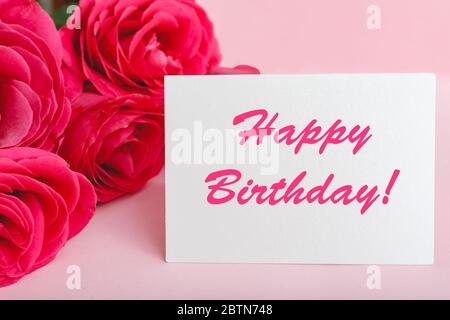 Felice testo di compleanno sulla carta in bouquet di fiori su sfondo rosa. Consegna fiori, carta di congratulazioni. Biglietto d'auguri in rosa rossa Foto Stock