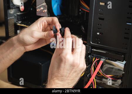 Man ripara un'unità di sistema del computer, cambia parti, scheda video e disco rigido. Ripristino guidato del computer Foto Stock