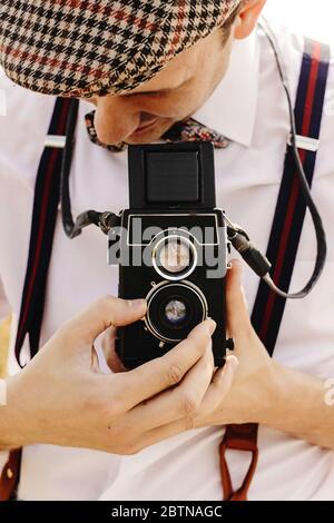 elegante hipster uomo che guarda e tiene la macchina fotografica di medio formato in campo soleggiato di girasole Foto Stock