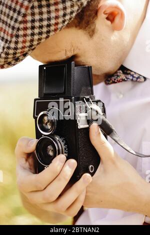 elegante hipster uomo che guarda e tiene la macchina fotografica di medio formato in campo soleggiato di girasole Foto Stock
