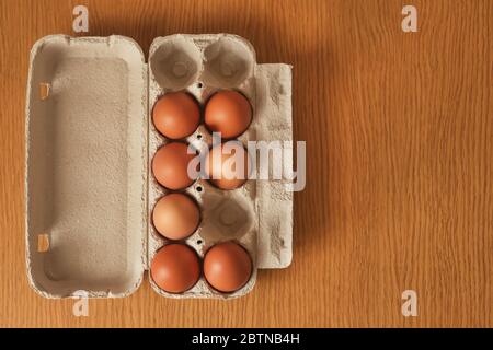 Uno sfondo di uova di pollo marroni in una scatola di cartone del negozio, che si trovano su un tavolo di legno. Foto Stock