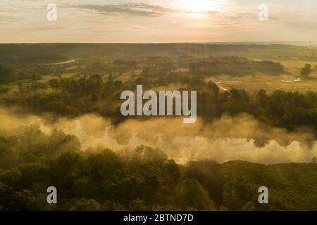 Nebbia sul fiume nei primi raggi del sole all'alba tra la foresta nel parco naturale. I primi raggi del sole dell'alba illuminano la nebbia luminosa sul fiume. Foto Stock