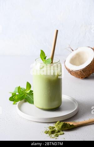 Tè freddo verde matcha in vetro con latte di cocco guarnire la menta su sfondo bianco. Primo piano.formato verticale. Foto Stock