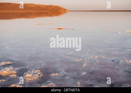 Lago salato rosa al tramonto. La superficie dell'acqua riflette la montagna Foto Stock