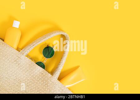 Giallo estivo luminoso piatto su sfondo colorato con sacco di paglia di vimini, tubi e bottiglia con crema solare, occhiali da sole verdi. Ombre e luci dure. Foto Stock
