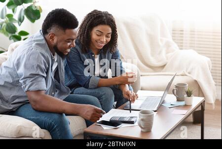 Sorridente coppia nera che discute l'importo totale delle loro spende a casa Foto Stock