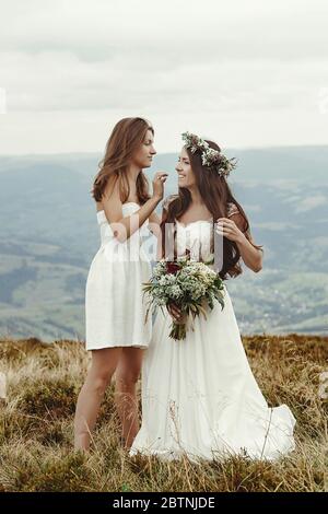 elegante sposa che aiuta a preparare una sposa splendida, matrimonio boho, cerimonia di lusso in montagna Foto Stock