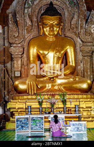 Una donna che prega di fronte A UNA grande statua di Buddha al Tempio di Htilominlo, Bagan, Regione Mandalay, Myanmar. Foto Stock