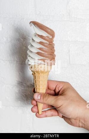 Tenere a mano un cono di cioccolato e gelato a vortice alla vaniglia Foto Stock