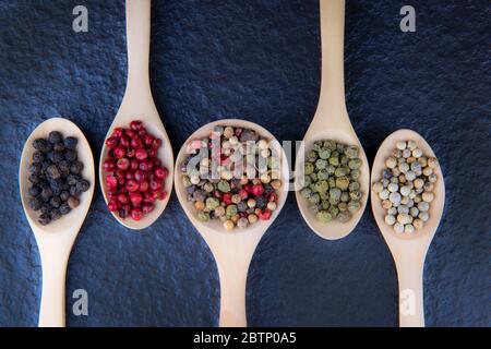 Piatto di 5 tipi di pepe in un cucchiaio di legno, posto per la posizione su uno sfondo nero, sano concetto di cibo Foto Stock