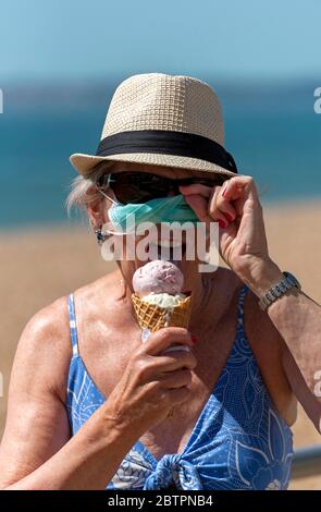 Southsea, Portsmouth, Inghilterra meridionale, Regno Unito. Maggio 2020. Donna che mangia gelato mentre indossa una maschera protettiva durante l'epidemia di Corvid-19 Foto Stock