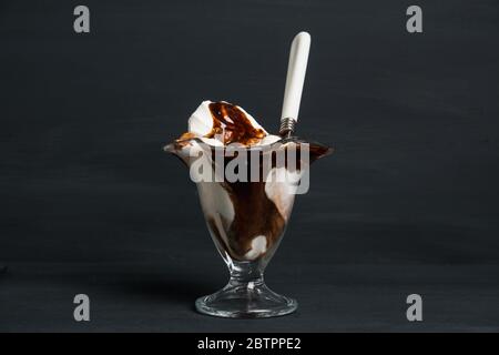 Gelato alla vaniglia con condimento al cioccolato su fondo di legno. Profondità di campo poco profonda. Foto Stock