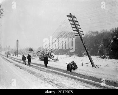 Distruzione della neve nel sud dell'Inghilterra. Poli del telegrafo soffiati. Il peggior caos della grande tempesta di neve che ha imperversato sull'Inghilterra meridionale è stato causato nel distretto di Lyndhurst della New Forest, dove i cavi telefonici sono stati abbattuti mentre gli alberi caddero, tagliando le comunicazioni in tutte le direzioni. Le strade principali sono state bloccate e il quartiere è caduto nel buio dalla rottura dei cavi di alimentazione. Foto mostra, telegrafo fili che si intralcia sulla neve coperta Lyndhurst Road come il sondaggio lascia a un angolo acuto. 8 dicembre 1937 Foto Stock