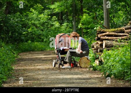 Donna seduta vicino baby buggy al parco ombreggiato e libro di lettura. 9 giugno 2019. Kiev, Ucraina Foto Stock