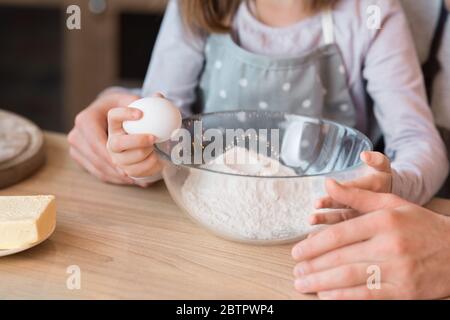 Bambina che coglie l'uovo alla ciotola, aiutando il padre con la pasta da cucina Foto Stock