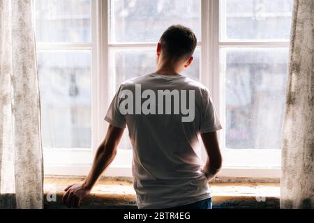 Un giovane irriconoscibile si alza vicino alla finestra in giornata di sole. Foto Stock