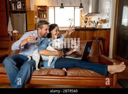 Coppia felice e cane da compagnia videochiama gli amici utilizzando il laptop. Uomo e donna in linea che chiacchiera celebrando l'allentamento delle restrizioni del coronavirus. Speranza e po Foto Stock