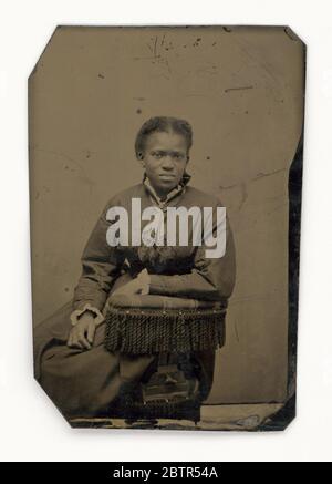 Tintype di una donna. Una tintype di una donna afro-americana non identificata seduta su una sedia e appoggiata sulla sedia con il suo avambraccio sinistro. Indossa un abito a maniche lunghe con una sciarpa da collo. Foto Stock