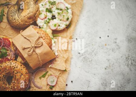 Bagel con prosciutto, formaggio cremoso, hummus, rafano avvolto in carta da forno marrone pronti per essere asporto Foto Stock