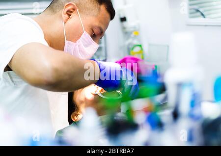 Medico maschile che esegue la procedura di estrazione con pinze che rimuovono il dente del paziente. Medico in maschera medica monouso. Foto Stock