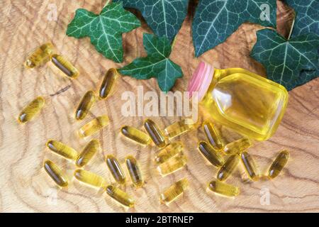 Capsule oblunghe gelatinose trasparenti di olio di pesce sono state sparse sullo sfondo di legno vicino alla bottiglia di olio. Grasso polinsaturo Omega-3-essenziale Foto Stock