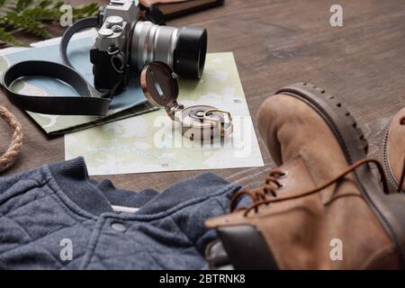 Primo piano di bussola e fotocamera fotografica su mappe poste su tavolo di legno con stivali e maglione, giacitura piatta Foto Stock