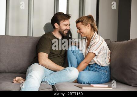 Foto di allegra coppia caucasica che ride e parla mentre si siede sul divano a casa Foto Stock