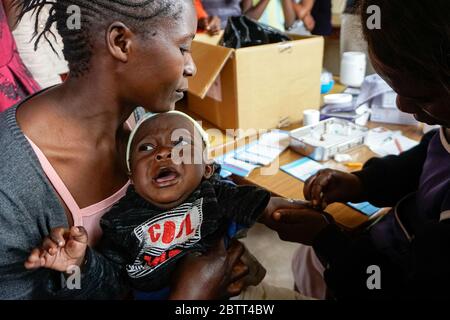 Rosalia Phiri detiene il suo bambino di nove mesi Joshua mentre riceve un vaccino contro il morbillo in una clinica istituita presso la Shine Charity a Lusaka, Zambia. Ogni sei mesi, gli operatori sanitari pubblici si trovano qui per le comunità, immunizzando i bambini idonei e fornendo altri servizi sanitari. (Prudence Phiri, GPJ Zambia) Foto Stock