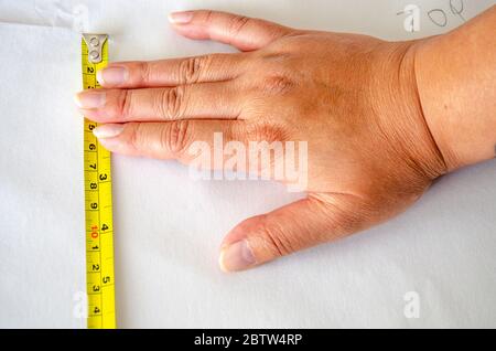 Close up view of a female hand holding a retractable metal measuring tape to measure a length of wallpaper. Foto Stock
