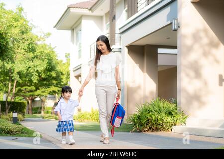 Felice madre asiatica e figlia studente asilo a piedi a scuola. Inizio delle lezioni. Primo giorno di autunno. La parentela o l'amore e il legame si allargano Foto Stock