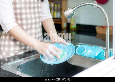 Chiudi mano di giovane donna asiatica attraente è lavando piatti al lavandino della cucina mentre facendo la pulizia a casa durante il soggiorno a casa utilizzando il tempo libero ab Foto Stock