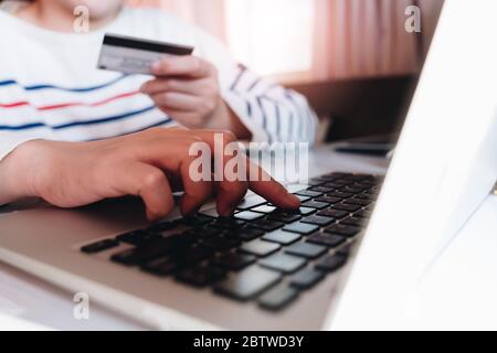 Primo piano con le mani che tengono la carta di credito, digitando sulla tastiera del computer portatile, Foto Stock
