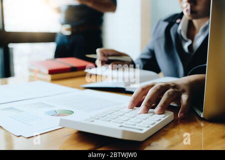 Donna di affari che usa la calcolatrice per fare la finanza matematica sulla scrivania di legno in ufficio Foto Stock