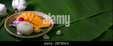 Primo piano vista del dessert tradizionale tailandese, mango con riso appiccicoso che serve su vassoio di legno con spazio per la copia e fiori decorati su foglie di banana Foto Stock