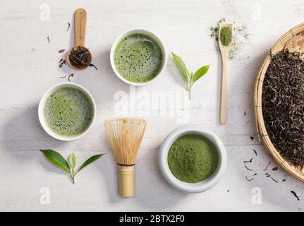 Tè verde matcha biologico in polvere in ciotola con frusta a filo e foglia di tè verde su tavola di pietra bianca, prodotto organico dalla natura per sano con trad Foto Stock