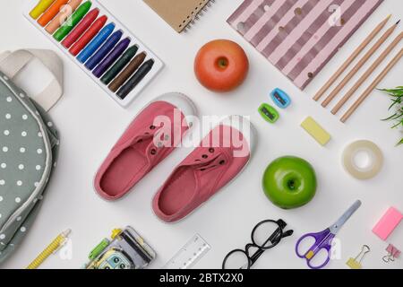 Piatto creativo di istruzione tavola bianca con zaino, libri per studenti, scarpe, pastello colorato, occhiali, isolato su sfondo bianco, concetto di Foto Stock