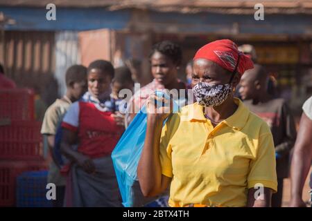 Donna nel mercato di strada, con maschera facciale in tessuto sarong africano per la protezione contro il corona-virus Foto Stock