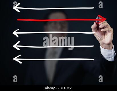 Uomo d'affari disegnando frecce in direzioni diverse, collezione di affari, studio shot Foto Stock