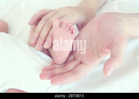 Messa a fuoco morbida e sfocatura dei piedi del bambino nella mamma della mano, effetto colore vintage stile Foto Stock