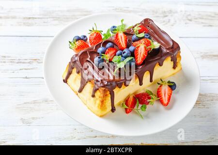 Cheesecake ucraino occidentale al forno di formaggio da cottage con glassa di cioccolato fondente sopra con mirtilli freschi, fragole, foglie di menta su una c bianca Foto Stock