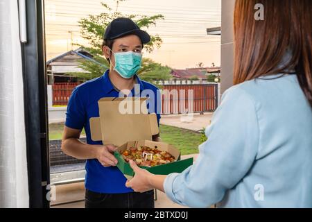 Consegna uomo consegna cibo pizza alla donna del cliente a casa, la gente deve indossare una maschera per prevenire la diffusione del coronavirus (Covid-19) Foto Stock