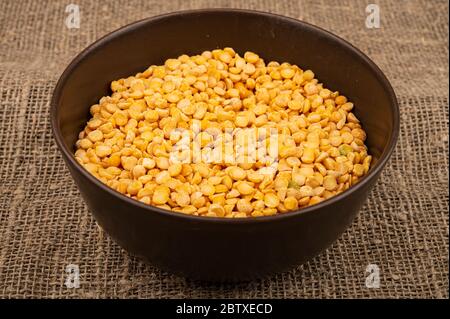 Piselli spezzati gialli in una ciotola in ceramica su uno sfondo di tela ruvida. Cereali tradizionali per la preparazione di zuppe e porridge. Primo piano Foto Stock