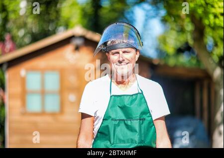 Buon giardiniere maschile che indossa casco utilizzando il rasaerba. Foto Stock