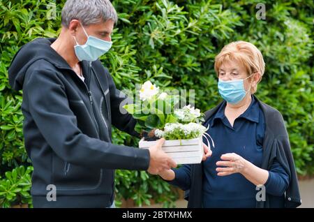 Uomo che consegna piante e fiori a donne anziane a casa in caso di epidemia di coronavirus. Foto Stock