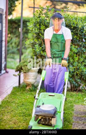 Buon giardiniere maschile che indossa casco utilizzando il rasaerba. Foto Stock