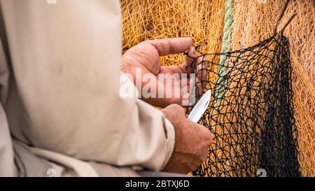 Primo piano di pescatore che ripara la rete da pesca con coltello. Foto Stock