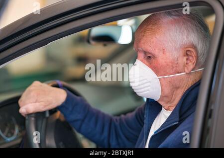 Uomo anziano che indossa una maschera facciale entrando nella sua auto a casa. Foto Stock