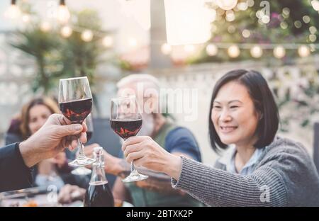 Buona famiglia mangiare e bere vino rosso a cena barbecue party all'aperto - mature e giovani cena insieme sulla terrazza Foto Stock